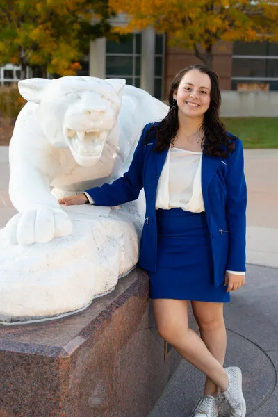 Woman with black hair and blue vest standing next to statue of mountain lion