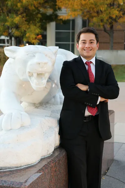 Man with brown hair and black suit standing next to mountain lion