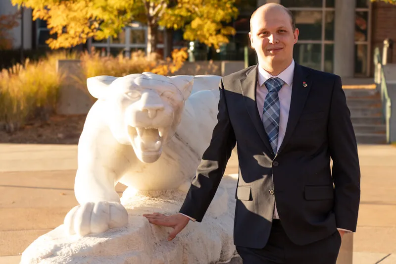 Bald man with black suit standing next to statue of mountain lion