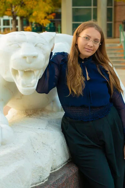 Woman with light brown hair and blue shirt standing next to statue of mountain lion