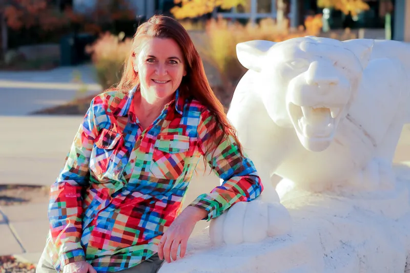Woman with red hair and colorful shirt standing next to statue of mountain lion