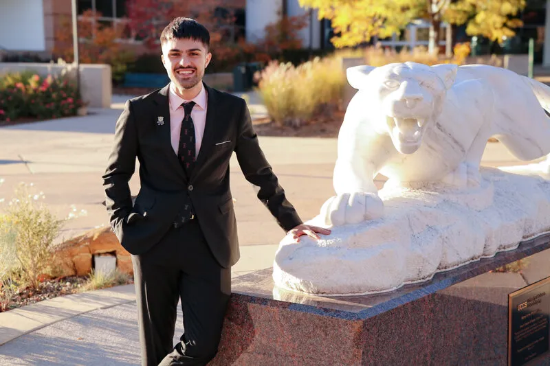 Man with black hair and black suit standing next to mountain lion